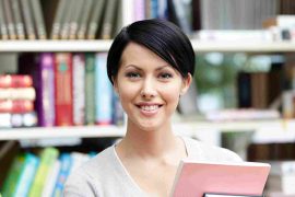 A teacher smiles while holding a book, representing English language learning resources.