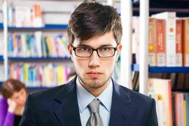 A suited man stands amongst bookshelves, representing Arthur Springs and higher education.